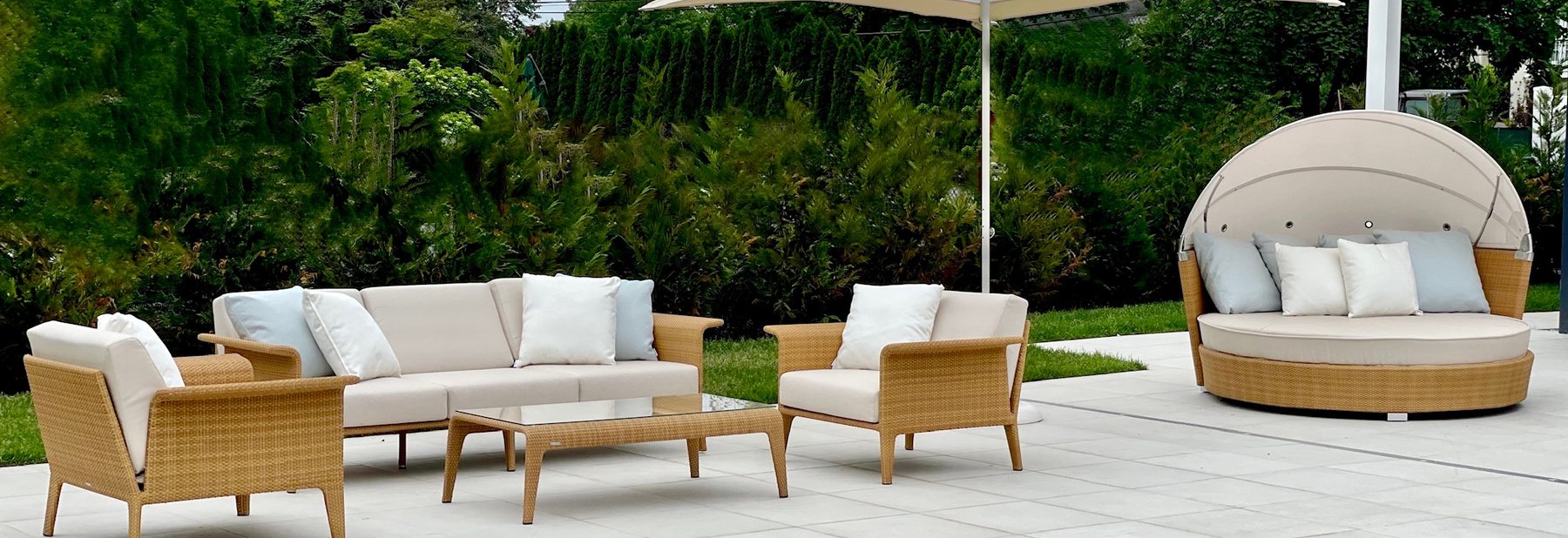 Woven lounge set, parasol and canopy daybed on a stone terrace against a green hedge