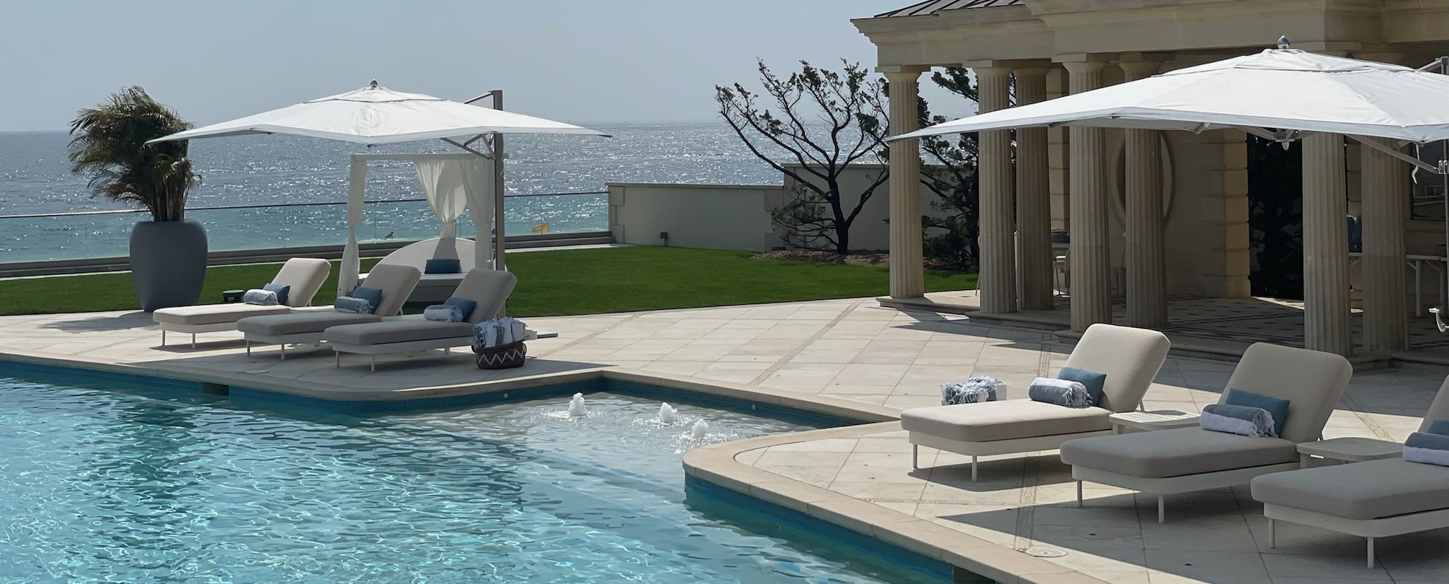 An oceanfront pool terrace with loungers, parasols and a colonnaded pavilion