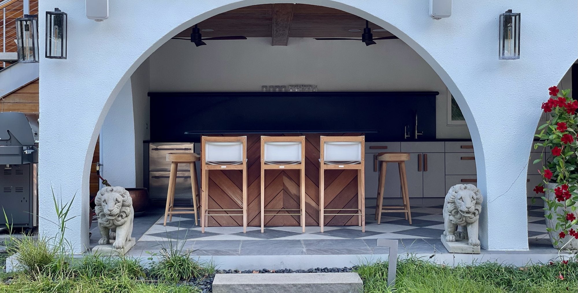 An arched loggia with teak bar stools at an outdoor kitchen