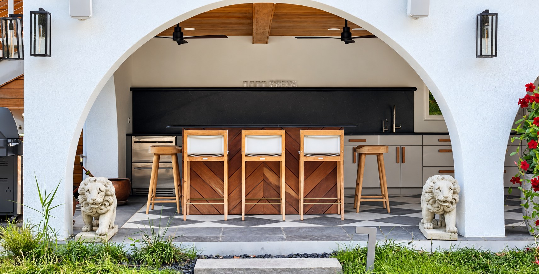 An arched loggia with teak bar stools at an outdoor kitchen