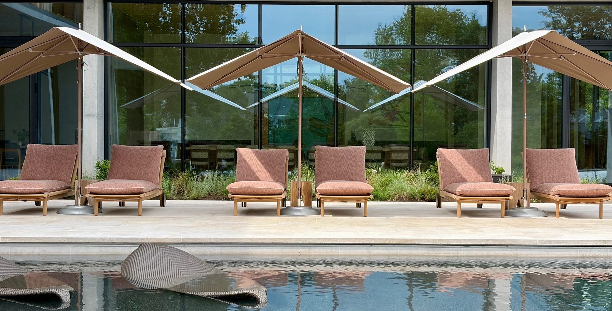 Six teak loungers under cantilever parasols beside a reflecting pool