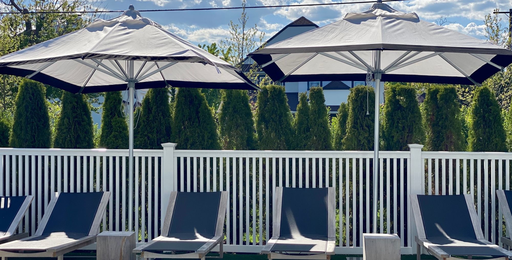 Navy loungers under parasols along a slatted pool fence